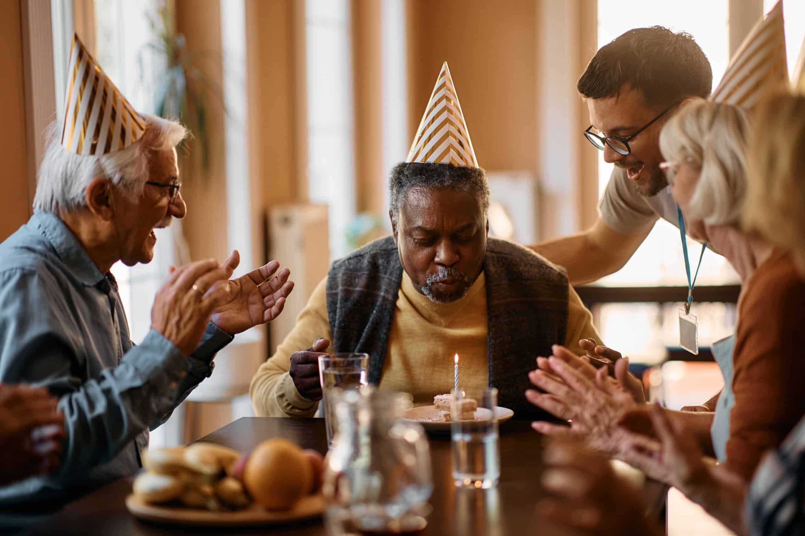 Black senior man blowing Birthday candle on cake in nursing home.