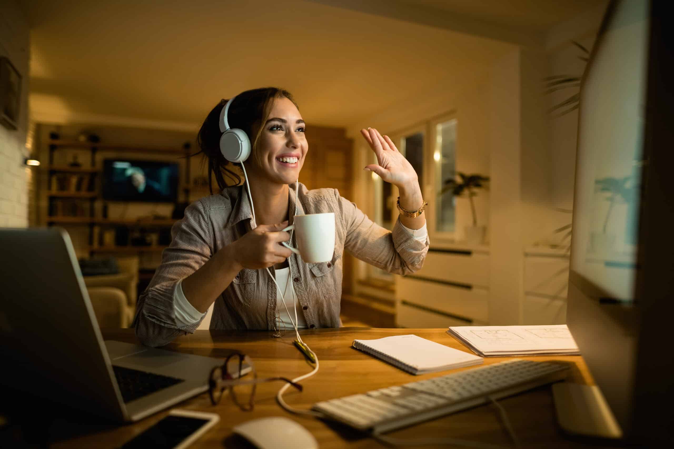 Happy woman with headphones making video call over computer at night.